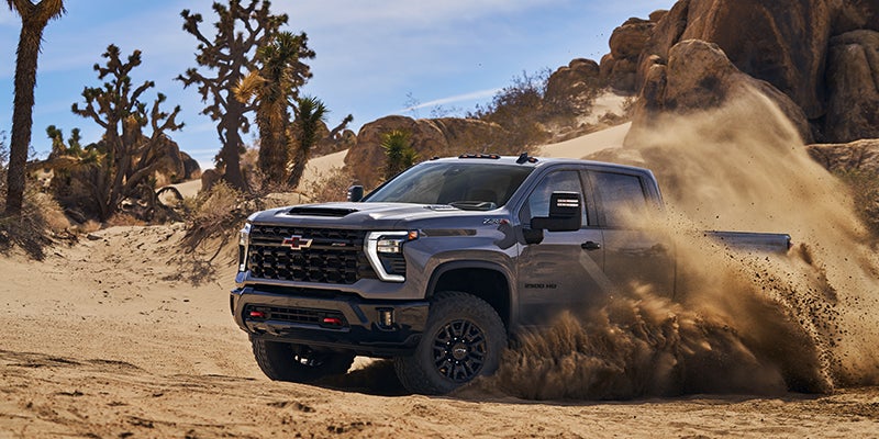 An all-new Granite Gray 2024 Chevrolet Silverado 2500 HD doing donuts in the sand of a desert. - Boyd GM Oxford, NC