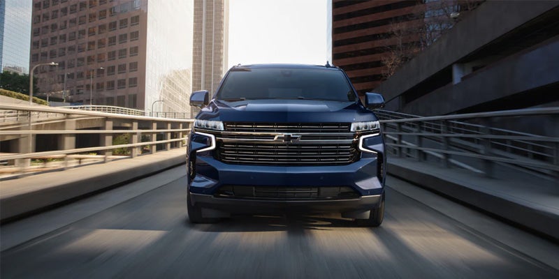 An all-new 2024 Midnight Blue Chevy Tahoe driving down a freeway exit ramp in the heart of downtown. - Boyd GM Oxford, NC