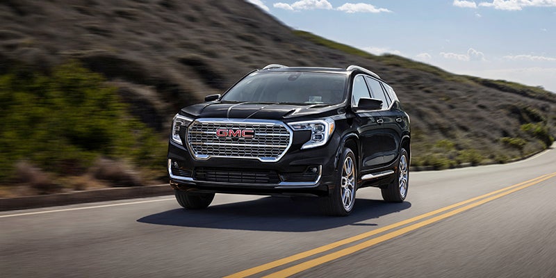 An all new 2024 Black GMC Terrain driving on a highway among the rolling hills. - Boyd GM Oxford, NC