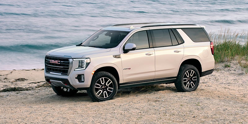 An all-new White 2024 GMC Yukon parked on the beach next to water. - Boyd GM Oxford, NC
