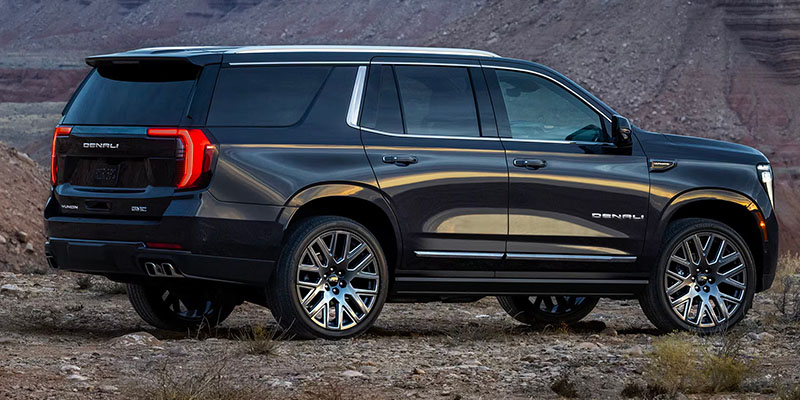 Rear passenger side view of a black 2025 GMC Yukon parked on rugged terrain