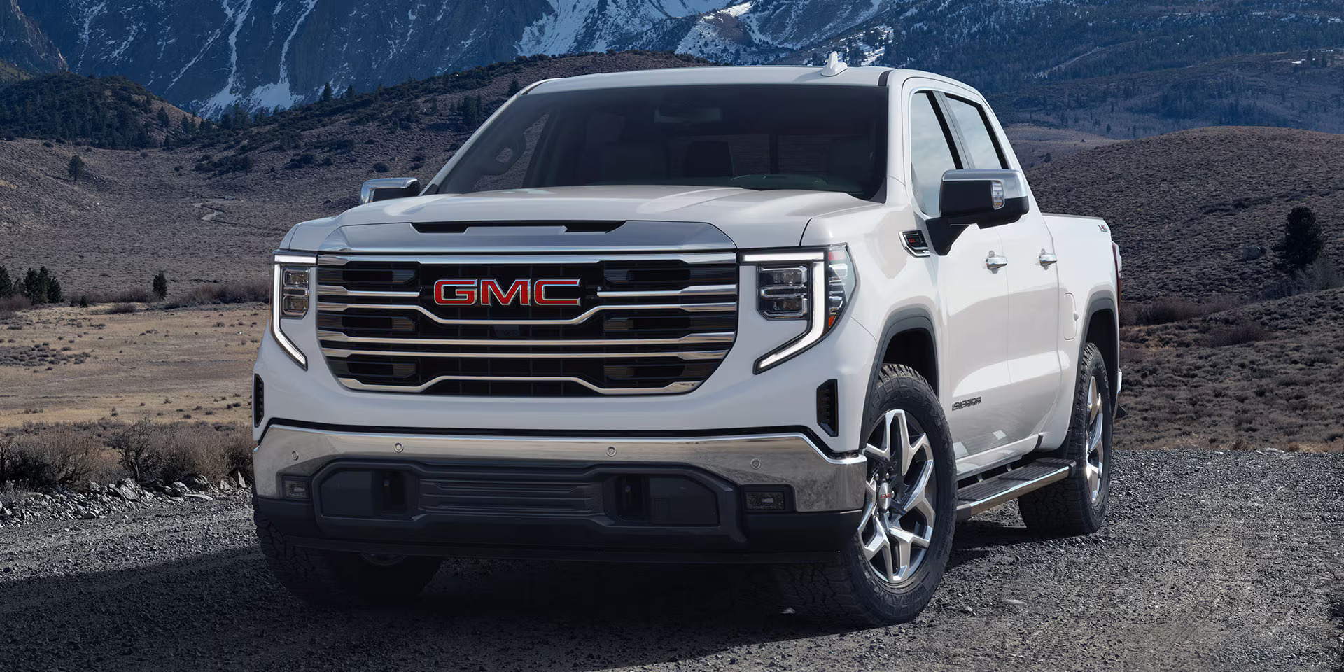 The 2025 GMC Sierra 1500 navigates a steep mountain road, highlighting its powerful presence in a natural setting.