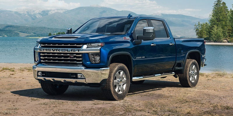 Blue Silverado HD parked in front of a scenic mountain and lake backdrop.