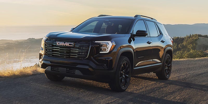 The image shows a 2026 GMC Terrain SUV in black, parked on a road with a scenic mountainous background.